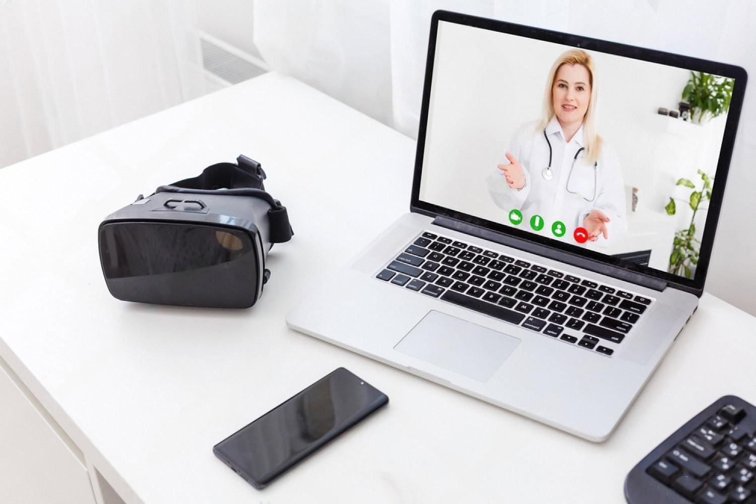 Workspace with laptop showing a doctor on video call, VR headset and smartphone beside it representing digital study tools